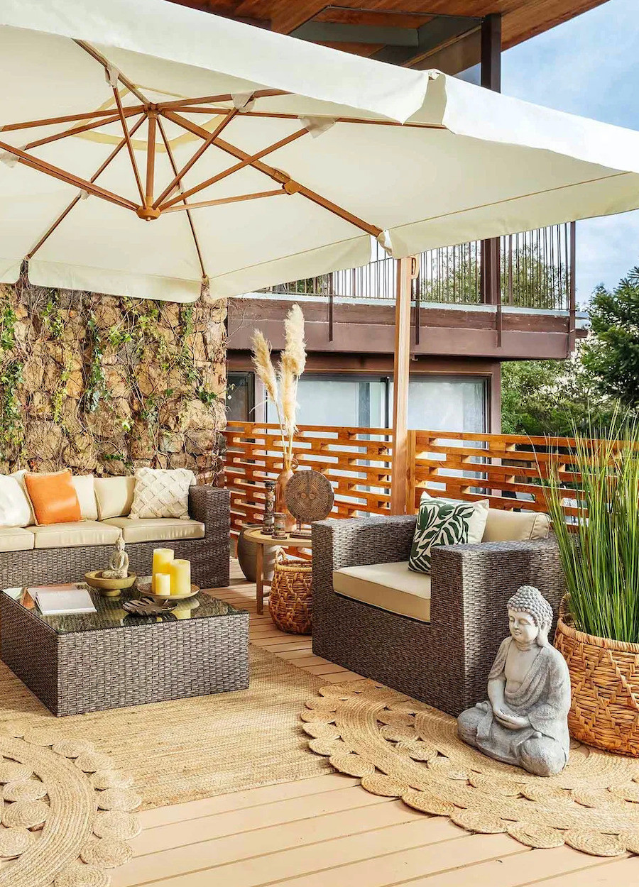Terraza de estilo boho chic con muebles de ratán, un quitasol blanco de madera, una alfombra redonda de yute y otra rectangular del mismo material.