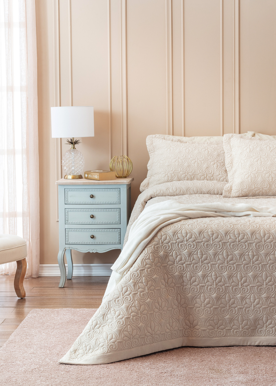 Dormitorio con pared color beige. Cama de 2 plazas con beige y crema. Mueble celeste estilo normando a un costado con cajones.