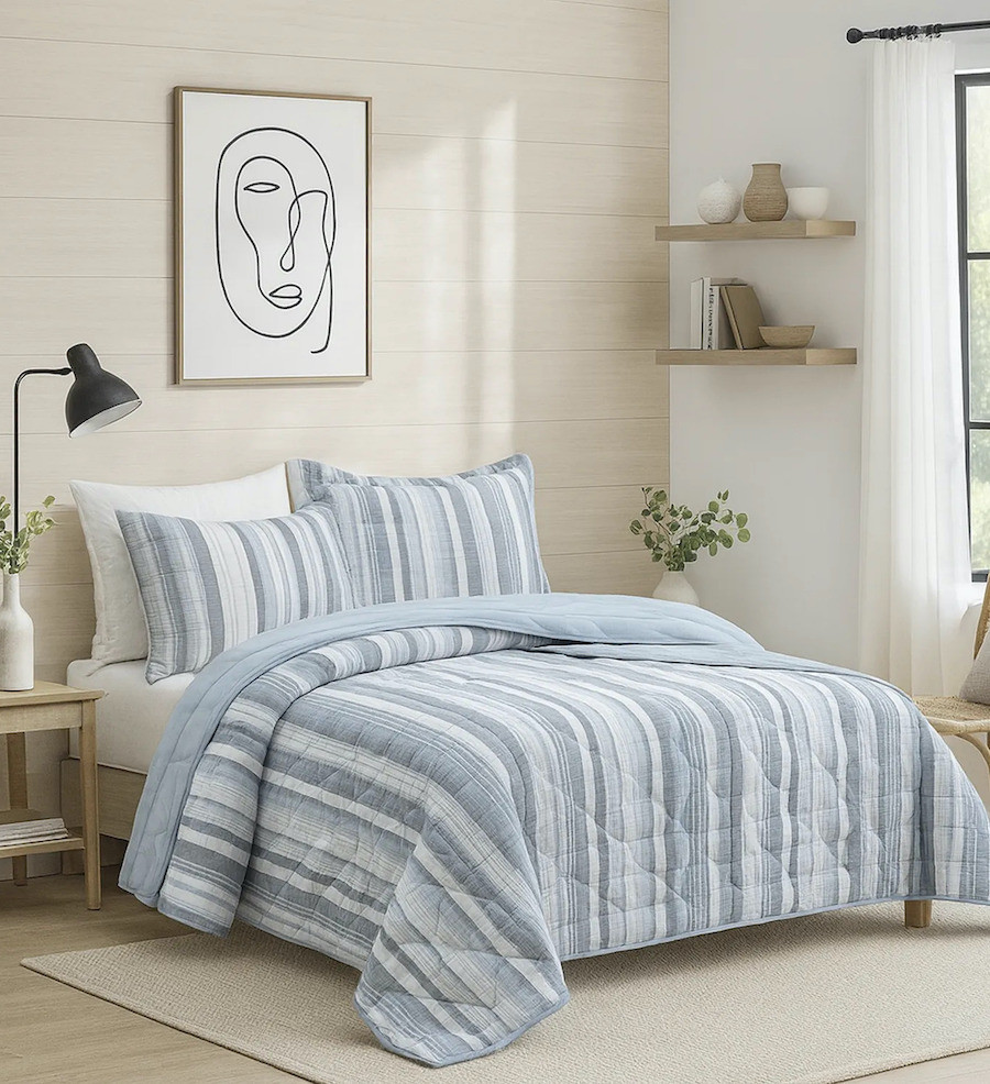 Dormitorio de estilo nórdico con un quilt de líneas blancas y celestes de distinto grosor. 