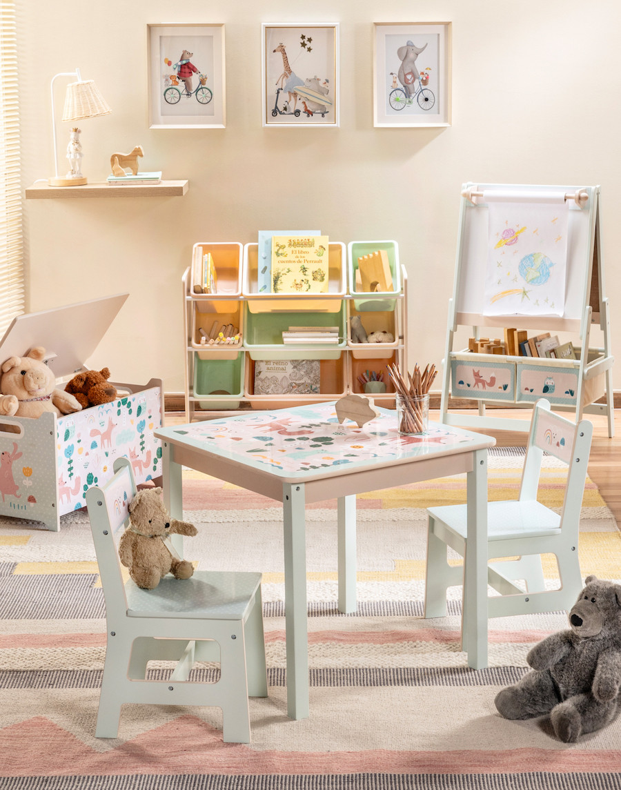 Habitación o dormitorio para niños en tonos pastel. Hay una pequeña mesa y sillas, un atril para pintar y dibujar, un baúl con juguetes, un mueble organizador, una alfombra de líneas rosadas, grises, blancas y amarillas; cuadros de animales en las paredes.
