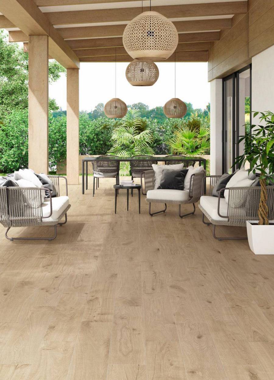 Terraza de una casa con suelo de porcelanato imitación madera. Sobre el suelo hay un juego de living de terraza de fibras naturales con cojines blancos. Del techo cuelgan 3 lámparas de fibras naturales.
