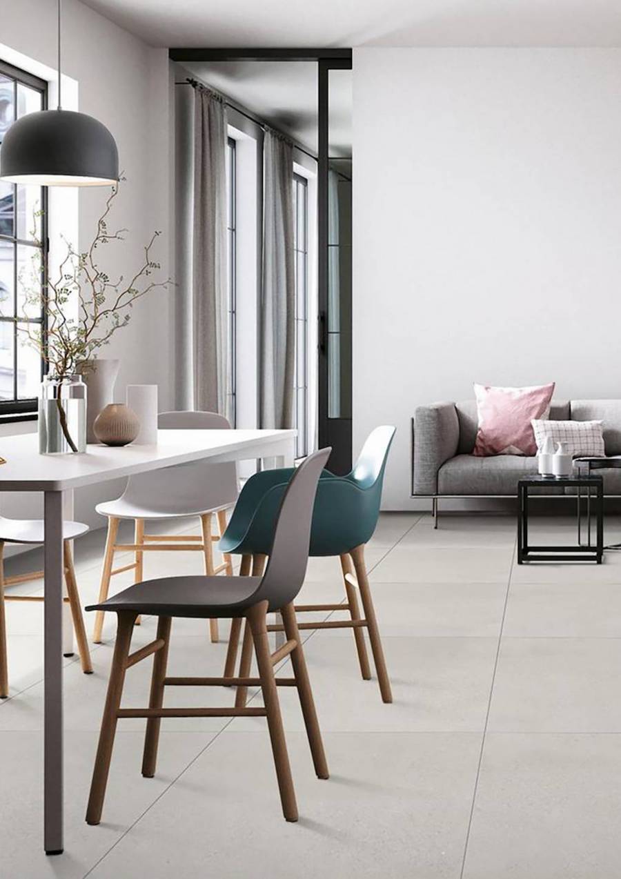 Living comedor con porcelanato de gran tamaño en el piso en tono beige claro. Hay una mesa de comedor blanca, sillas de colores y al fondo, un sofá gris con cojines de colores frente a una mesa de centro negra.