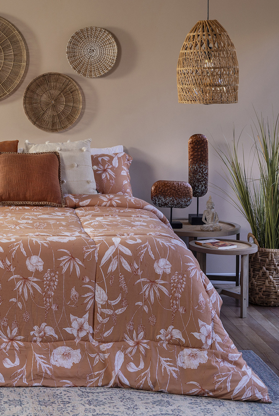 Dormitorio Boho chic con una cama con un plumón color salmón con diseño de flores y hojas blancas, cojines color crema y terracota. Al costado hay 2 mesas auxiliares que funcionan como velador, y un canasto con una planta de interior.