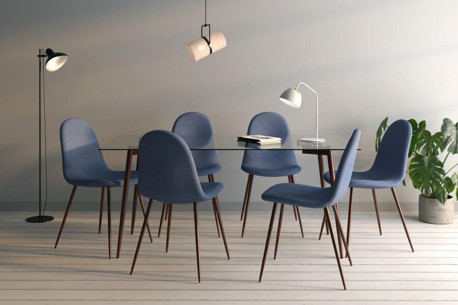 Bodegón ejecutivo. Mesa de comedor de vidrio con 6 sillas azules. Sobre la mesa hay una lámpara de escritorio blanca. Lámpara de techo blanca, tipo foco colgante, metálica, minimalista. Lámpara de pie negra, con pantalla metálica
