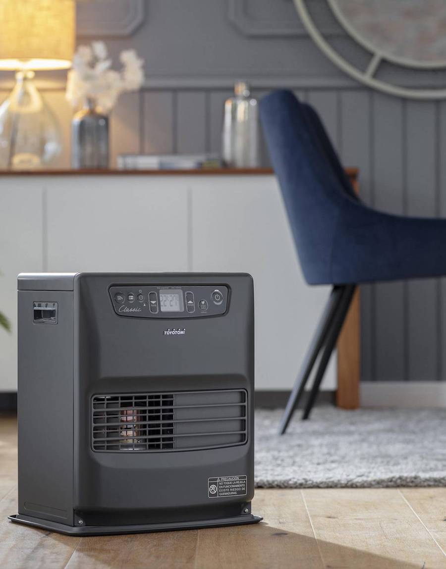 Estufa láser a parafina, de color negro. Ubicada sobre piso de madera, en un comedor. Atrás se ve una silla con tapiz azul y un mueble de madera con puertas blancas.