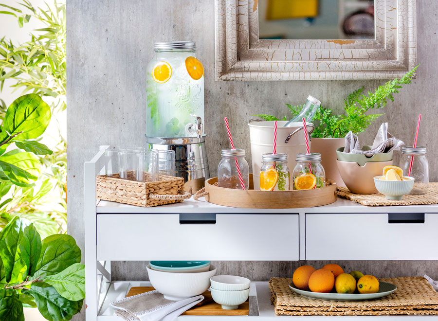 un carrito de cocina en un espacio al aire libre. Es blanco y tiene varios elementos de cocina y bebida sobre él.
