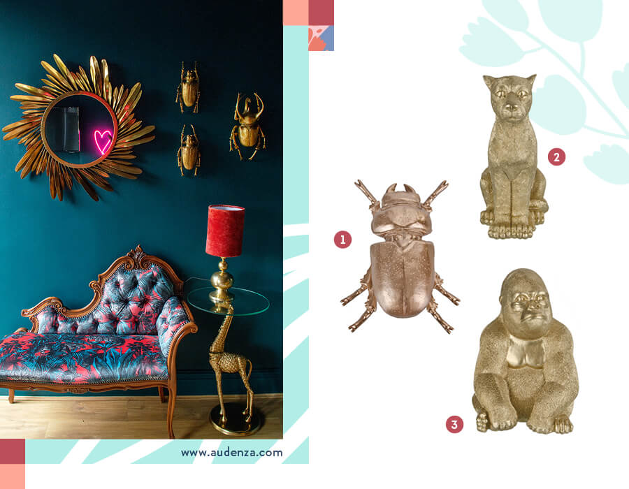 Figuras decorativas doradas Una imagen dividida en dos partes. En la izquierda, una ambientación con una muralla azúl petróleo, en la que están colgadas tres figuras de escarabajos dorados de adorno y también un espejo del mismo color. Hay un diván estilo poltrona con un estampado llamativo, y una mesita con forma de jirafa dorada. Sobre ella, hay una lámpara dorada con pantalla roja. La imagen de la derecha son tres objetos dorados de animales, un escarabajo, un puma y un gorila.