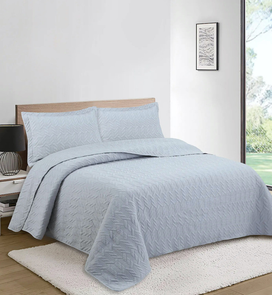 Dormitorio de paredes blancas con una cama con un quilt de color azul cielo. 