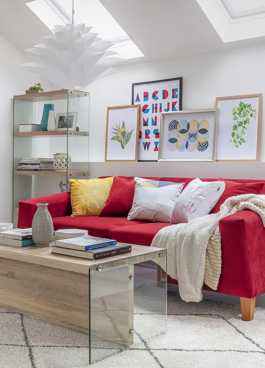 Living con la teoría del rojo inesperado. Gran sofá rojo con cojines blancos, amarillo y rojo. Mesa de centro de madera y vidrio, con repisa alta a juego