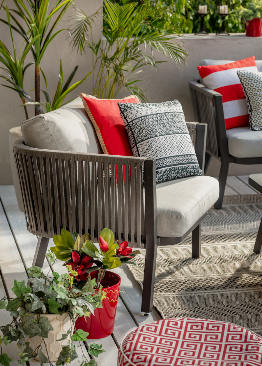 Muebles de terraza con la teoría del color rojo inesperado. Sitial negro con cojines gris claro, gris oscuro y rojo.