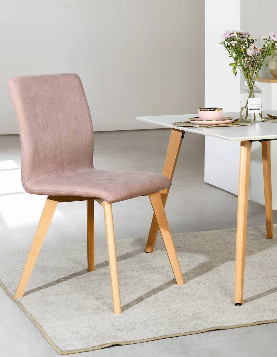 Comedor pequeño de patas de madera y superficie blanca junto a una silla de patas de madera clara y tapiz rosado pastel de terciopelo.
