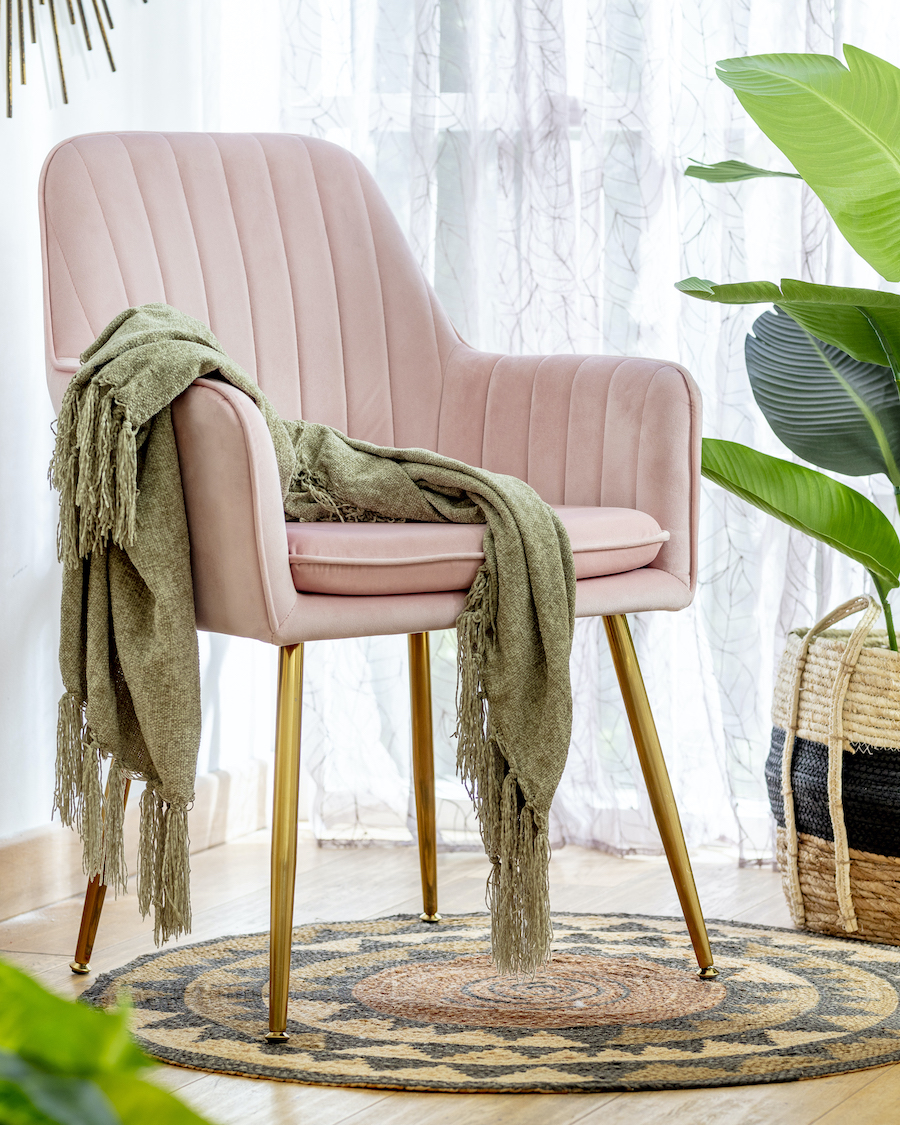 Silla rosada de terciopelo con patas delgadas y doradas. Sobre ella hay una manta color arena y debajo, una alfombra de yute estilo boho chic.