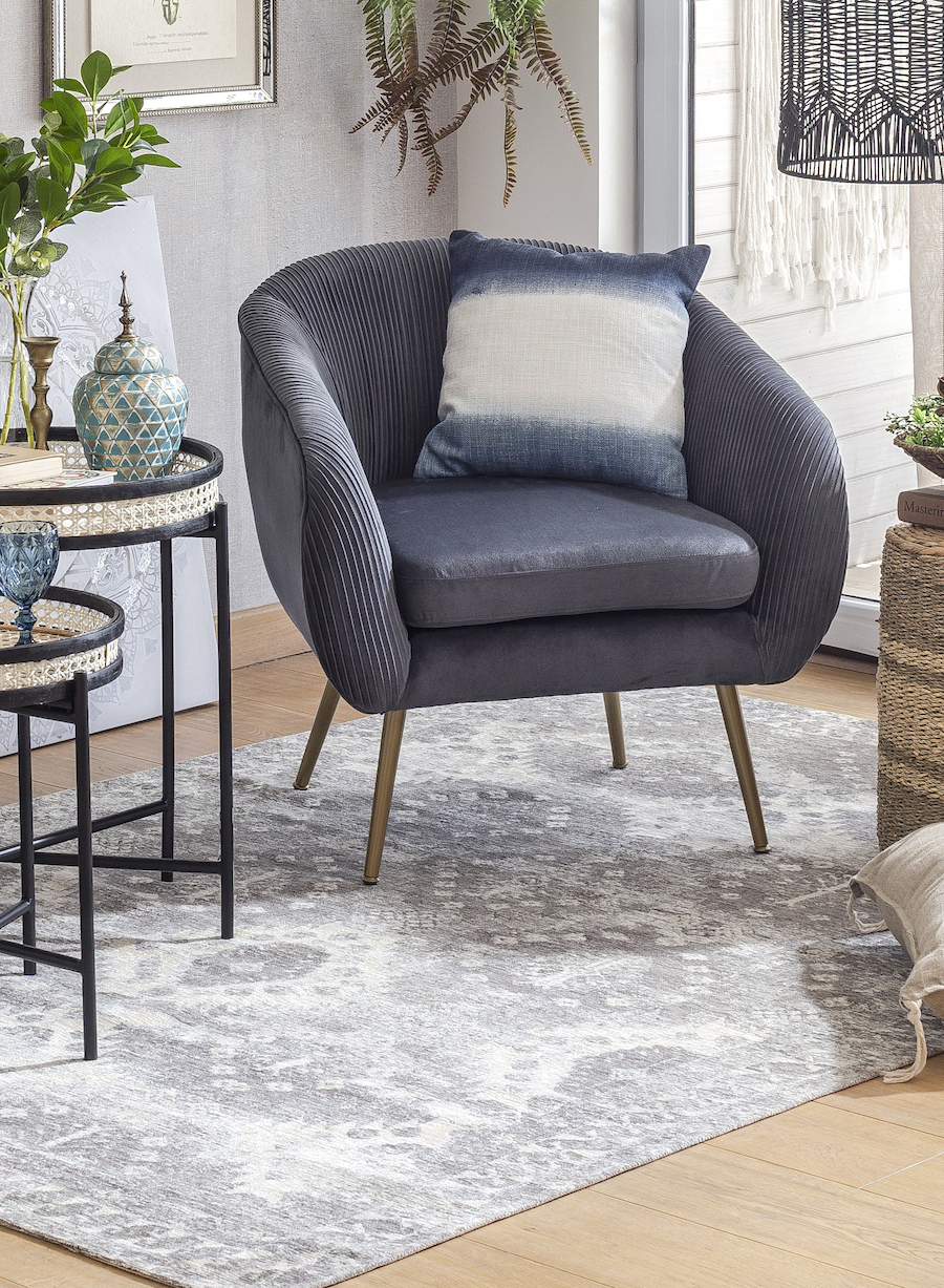 Rincón de una sala de estar con un tipo de alfombra oriental en tonos grises con una poltrona gris oscuro y decoraciones de estilo Boho chic, tales como cojines, mesas laterales, adornos, etc.