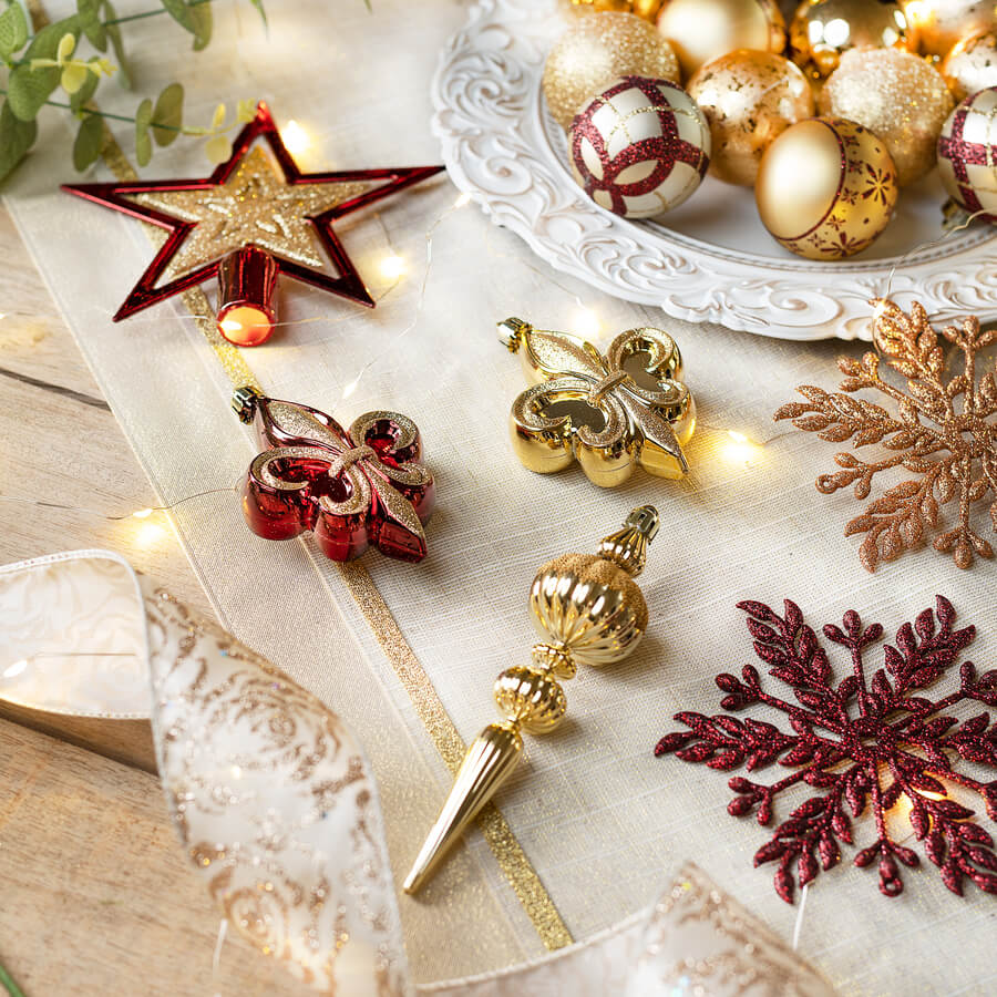 Detalle de una mesa de madera, con un camino de mesa beige. Sobre él hay adornos de navidad dorados con rojos, una bandeja con pelotas navideñas doradas y ramas de eucaliptus. Además hay una guirnalda de luces led y una cinta de tela beige con dorado