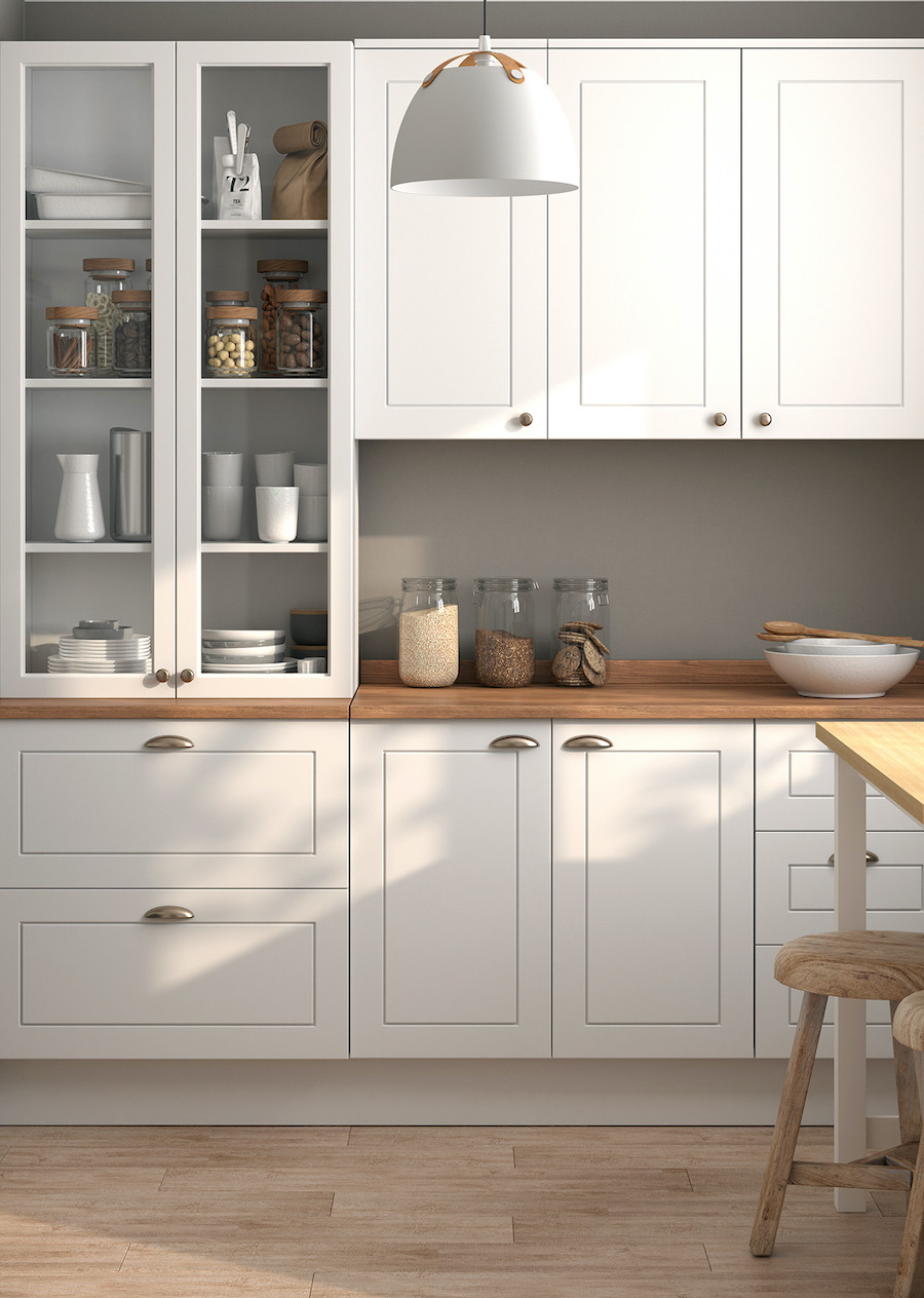 Cocina pequeña con muebles blancos, cubierta de madera, tiradores metálicos y frascos de vidrio y menaje en tonos neutros. La pared del fondo es gris.