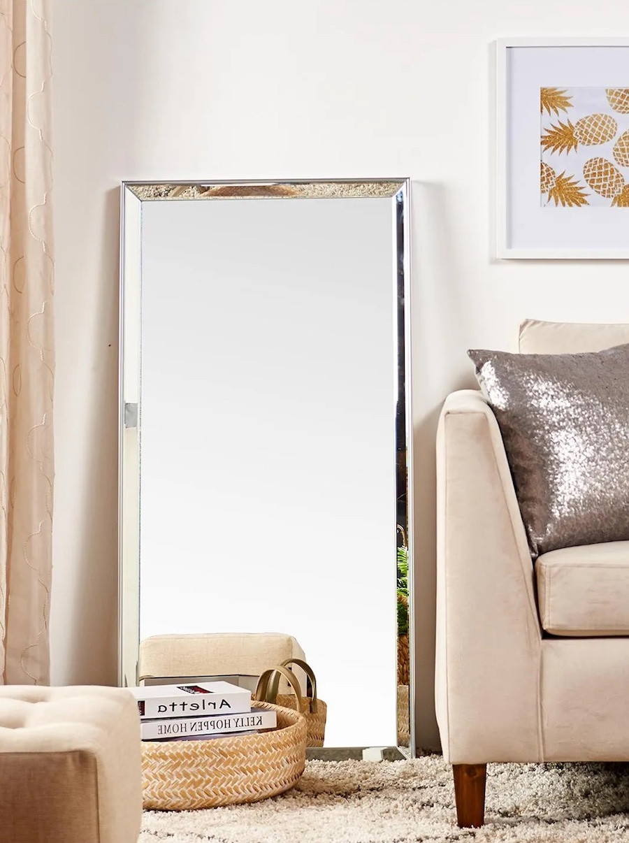 Sala de estar con un sofá beige junto a un gran espejo de cuerpo completo en el piso apoyado en la pared.