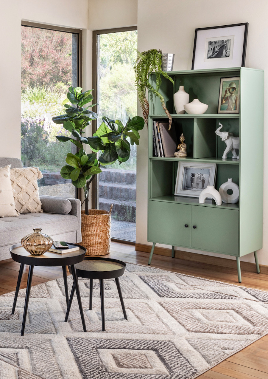 Living con un sofá gris, una alfombra de diseño geométrico gris y un estante verde menta con distintos adornos en tonos neutros, desde jarrones blancos hasta cuadros y figuras decorativas. 