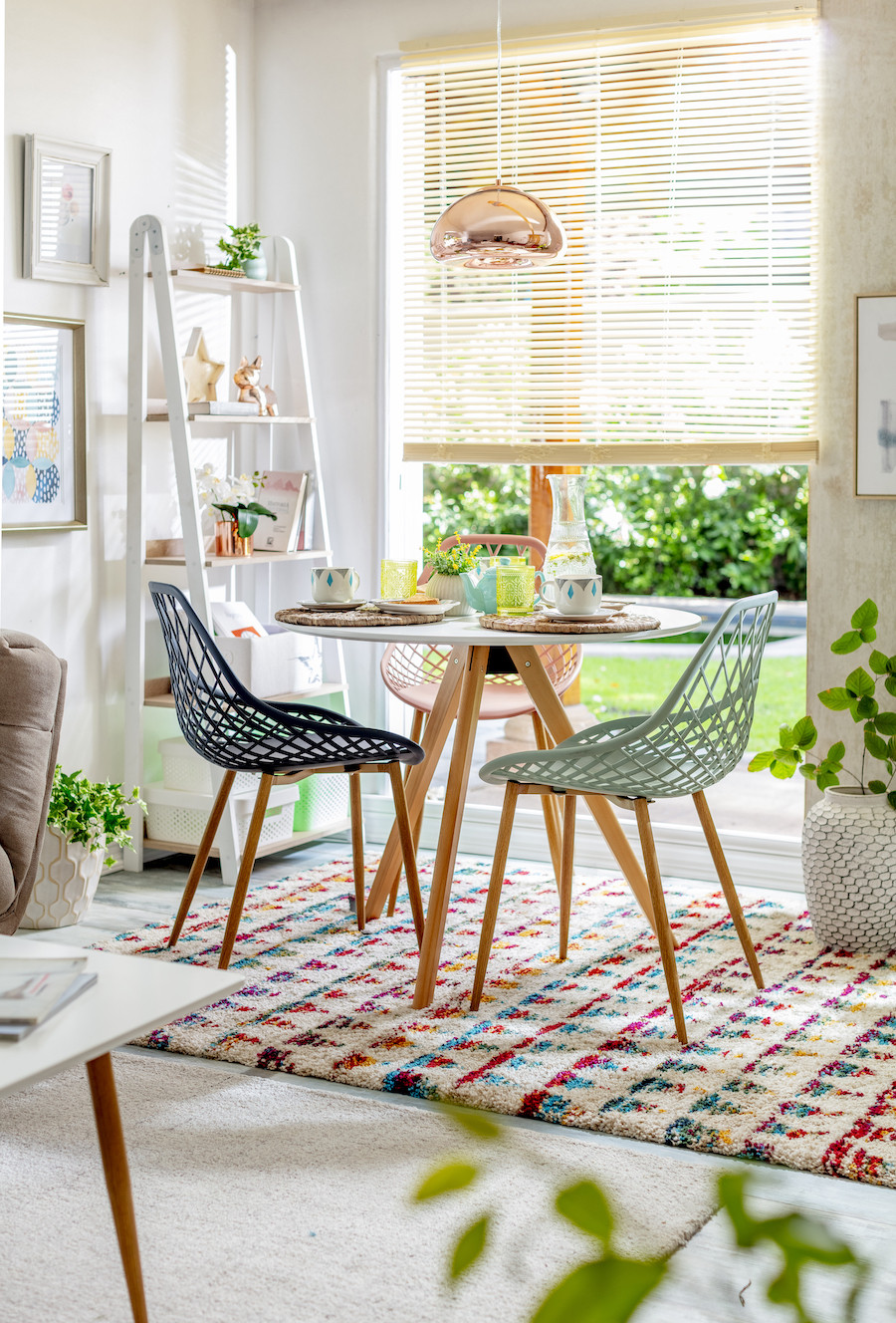 Comedor pequeño con mesa redonda y sillas modernas y coloridas de diseño, acompañado de alfombra colorida y luz cálida.