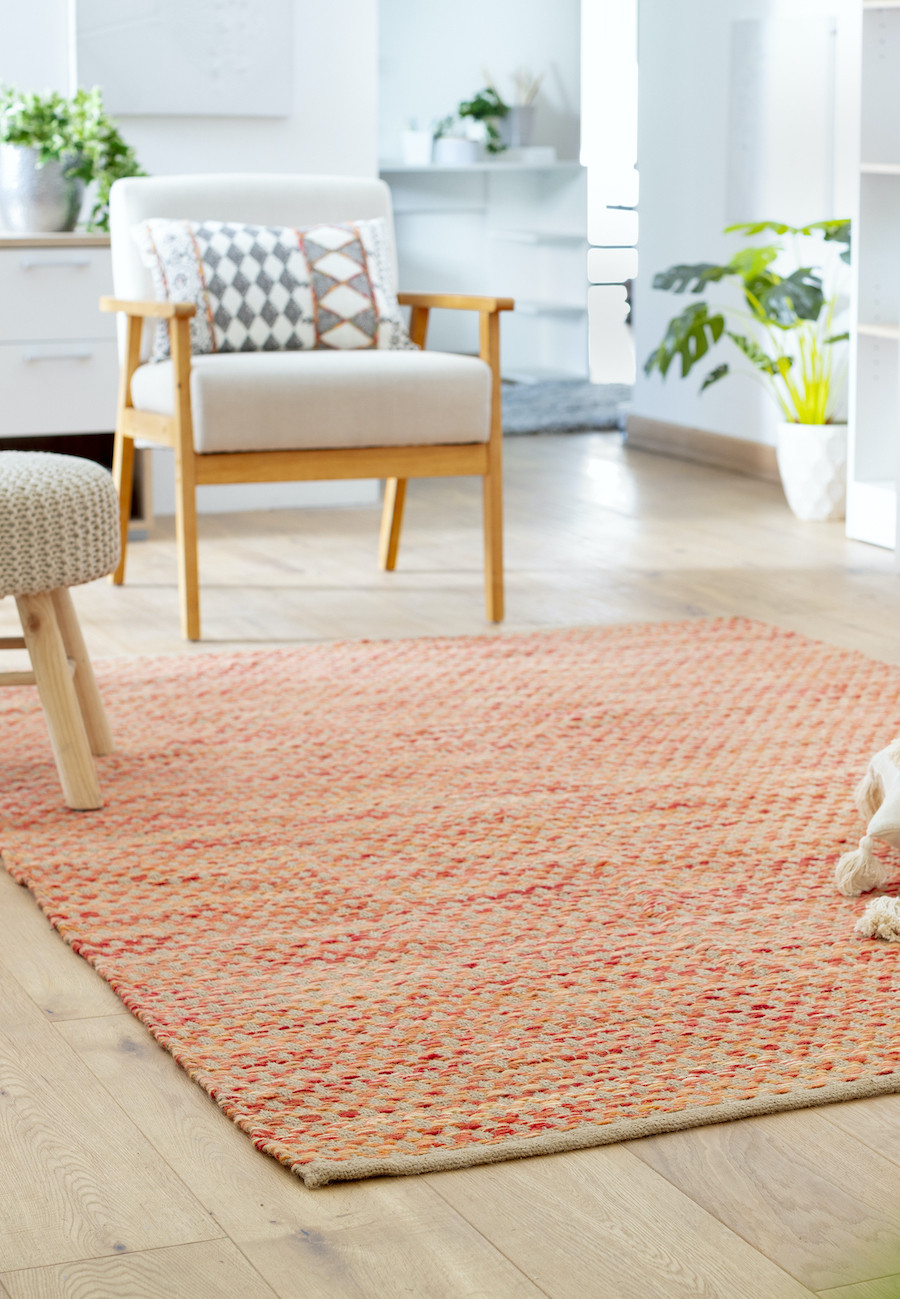 Alfombra jaspeada, color naranjo. Poltrona de madera con tapiz blanco, pouf tejido con patas de madera.