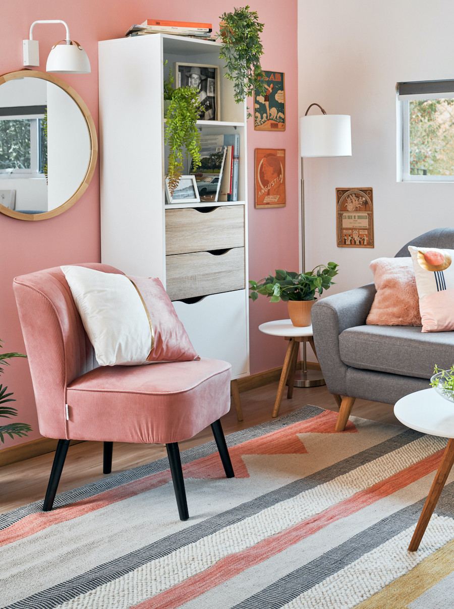 Living nórdico con poltrona rosada, sofá gris y alfombra geométrica en tonos blanco, gris y rosado.