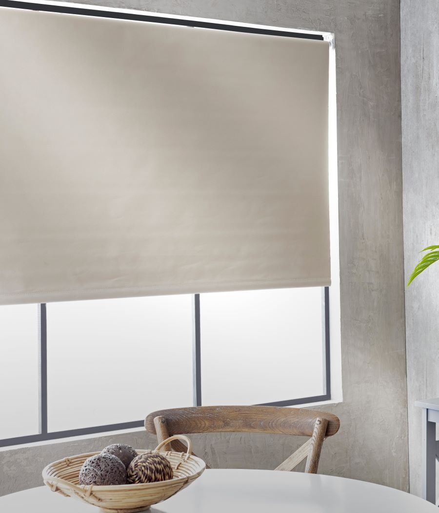 Cortina roller black out color beige sobre gran ventana con marco metálico negro. 