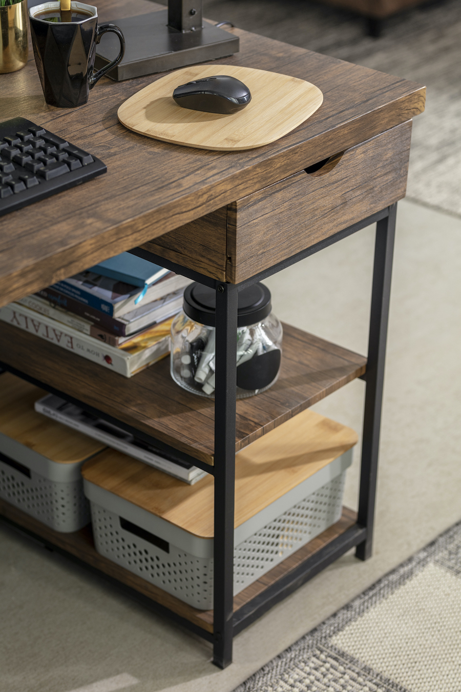 Detalle de un escritorio de estilo industrial, hay un cajón y dos estantes con libros, y cajas organizadoras.