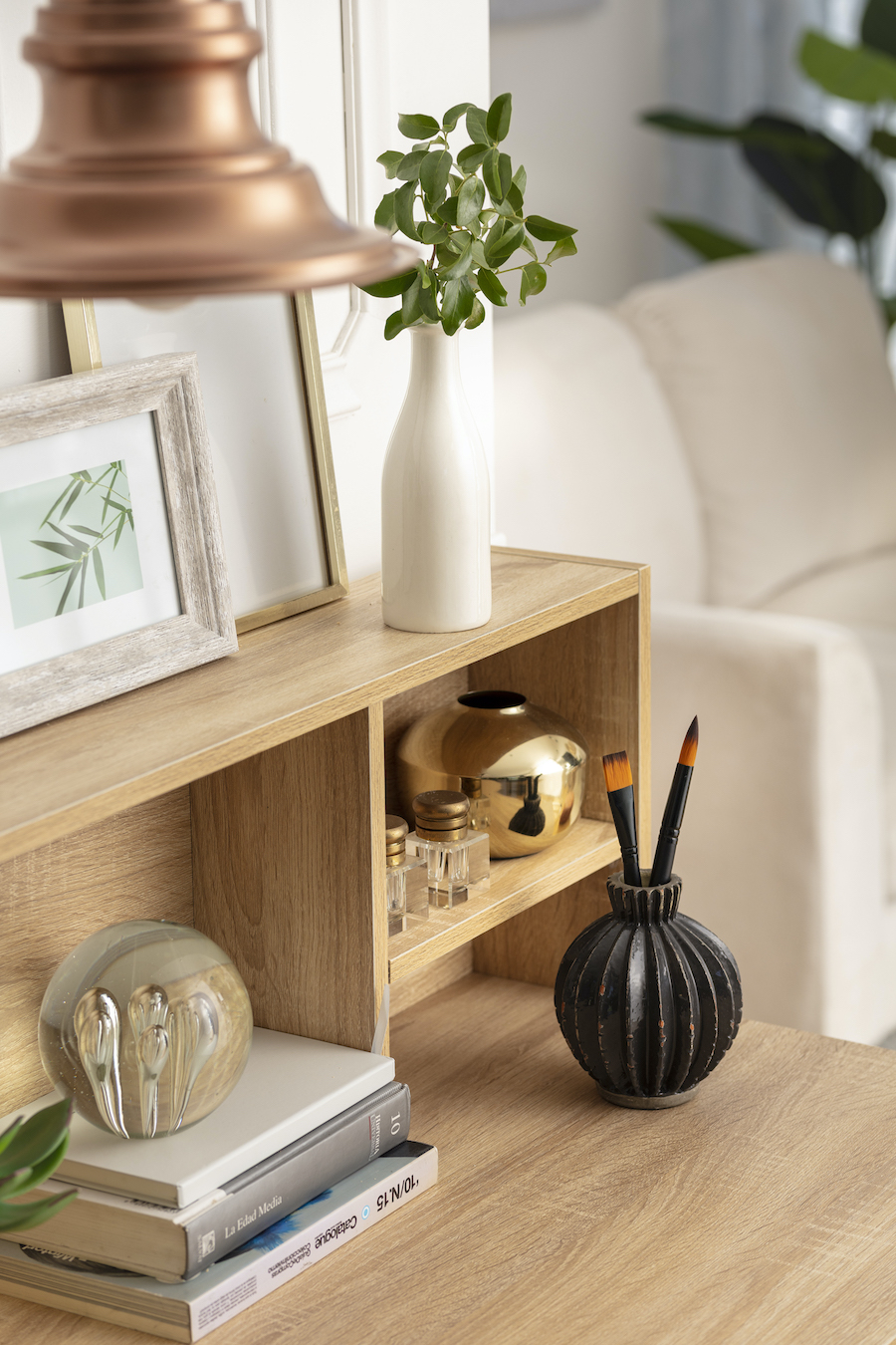 Esquina de un escritorio de madera clara con un florero, marco de foto con una ilustración y otros adornos.
