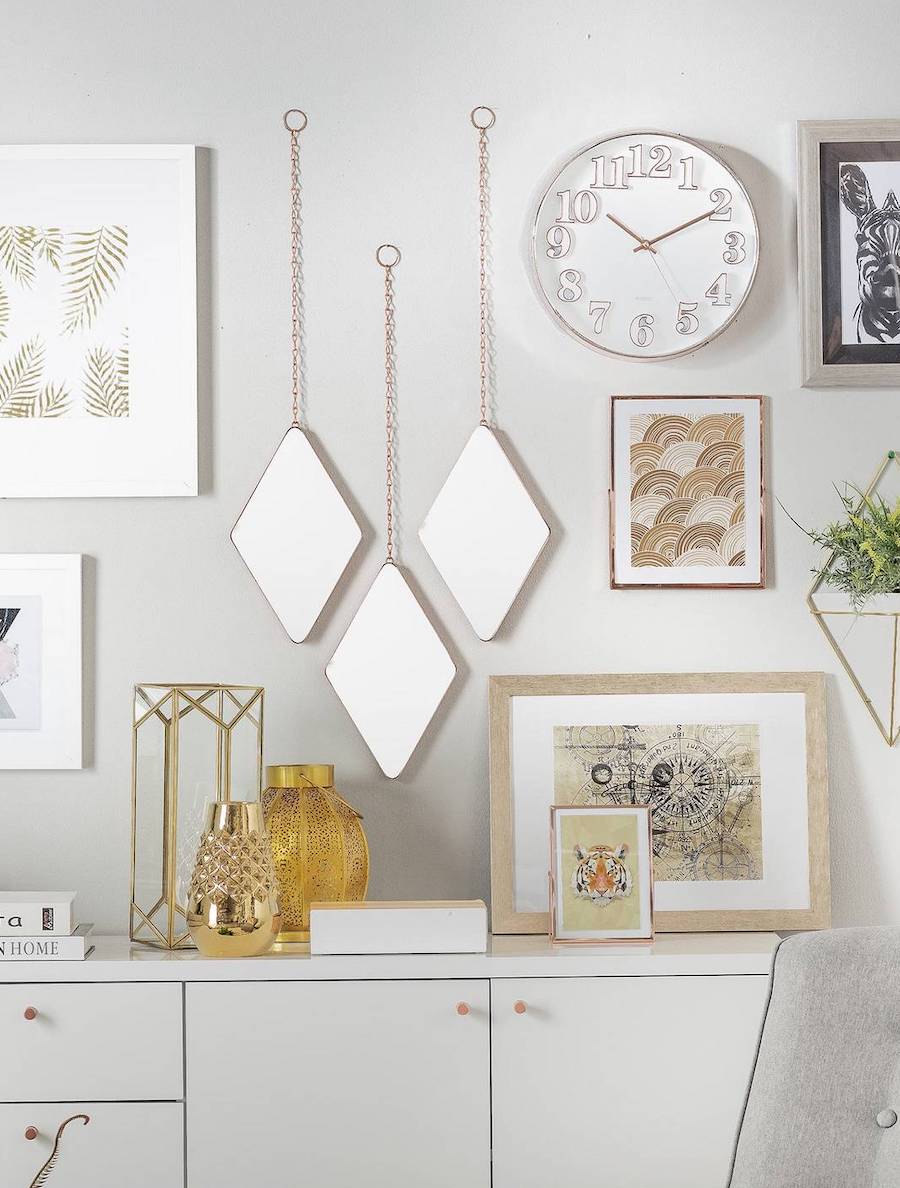 Pared gris con cuadros deco, un reloj blanco, espejos y un buffet blanco con más cuadros y adornos en tonos dorados.