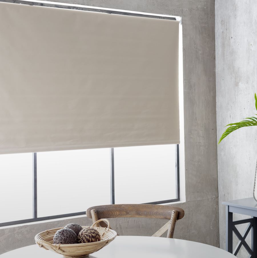 Comedor con gran ventana con marco negro. Lo cubre una cortina roller blackout color beige o crema. Muros grises. Comedor con mesa redonda y silla de madera