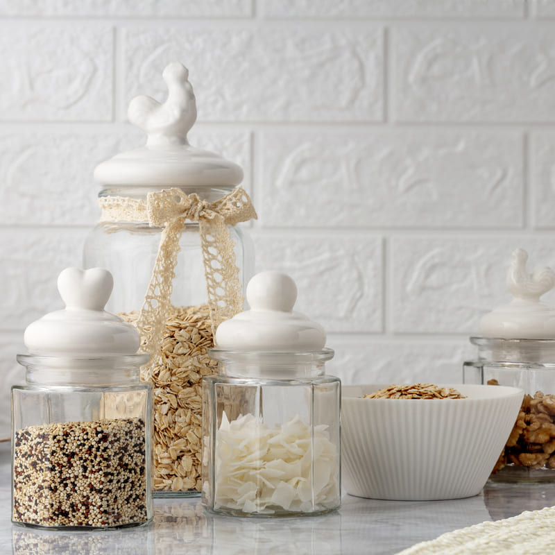 Frascos de vidrio con tapas de cerámica blanca con forma de animales y bowls blancos con ingredientes.