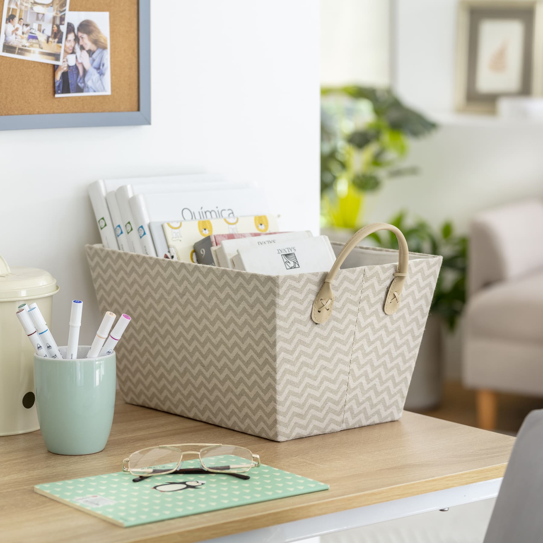 Canasto rígido de tela con patrones en zig zag gris y beige con asas, contiene libros y está sobre un escritorio de madera.