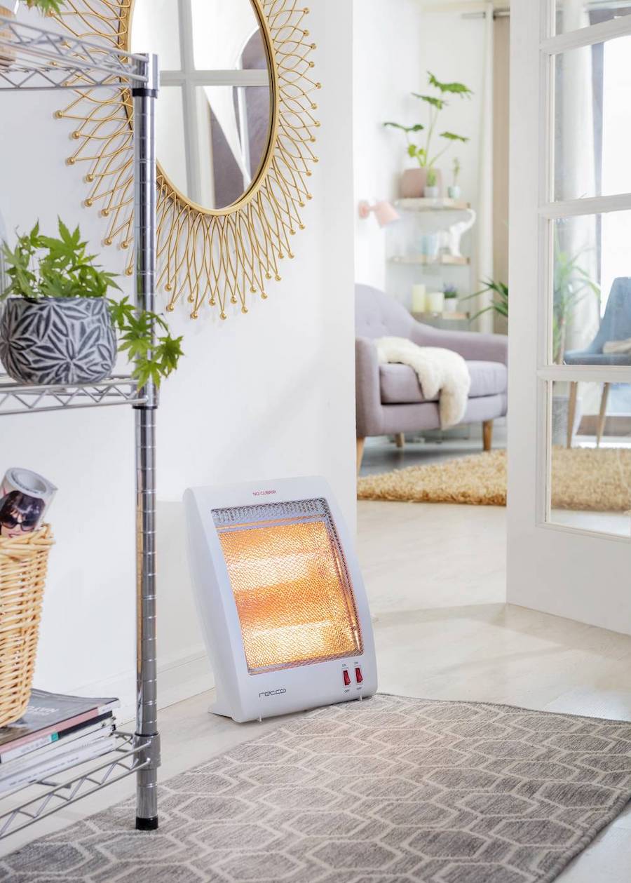 Calefactor halógeno blanco, disponible en Sodimac. Está en una sala de muros blancos, junto a una repisa metálica.