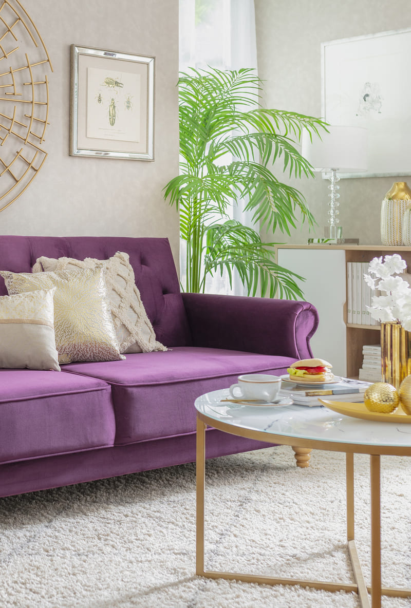 Living con un sofá velvet morado con una mesa de centro redonda con cubierta blanca y patas de metal dorado.