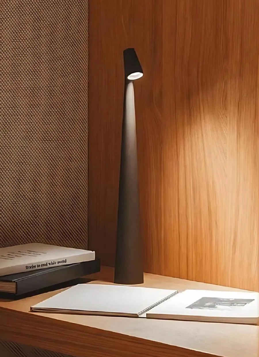 Detalle de un escritorio con libros y una lámpara inalámbrica negra con forma escultural.