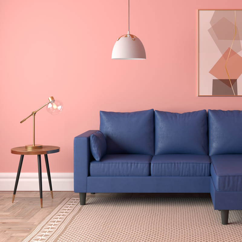 Living con sofá de tres cuerpos color azul marino. Pared rosa y suelo de madera, con una alfombra con patrones beige y crema. Al lado del sofá hay una mesa lateral de madera redonda y, sobre ella, una lámpara estilo vintage moderno.