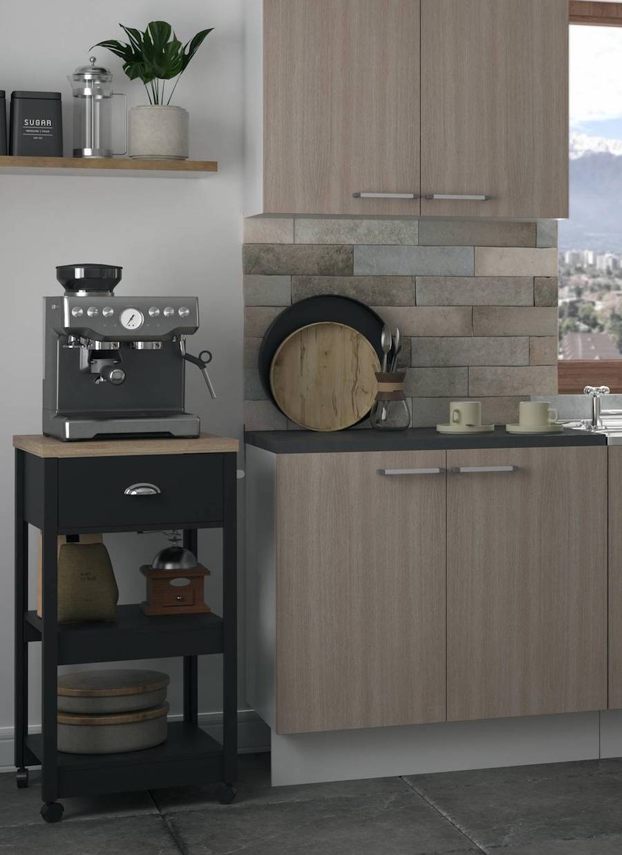 Isla de cocina pequeña, de color negro, dos repisas y un cajón. Tiene una cafetera y está junto a un mueble de cocina de madera oscura.