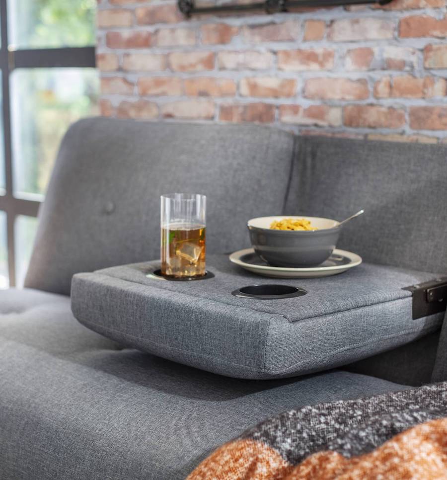 Futón gris con una sección de su respaldo reclinable -la del centro-, sobre él hay un vaso con bebida y un bowl con cereal.
