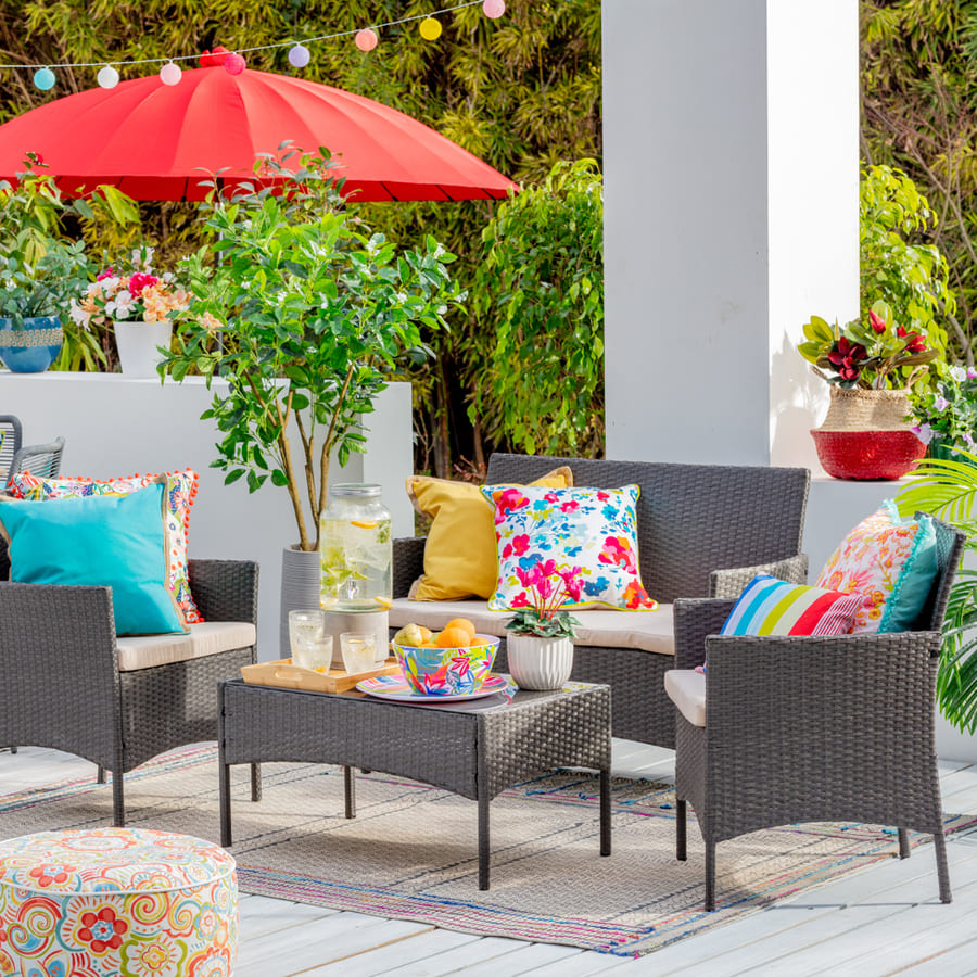 Una alfombra de fibras naturales con franjas con patrones, debajo de un juego de living de terraza oscuro, al fondo hay un quitasol rojo.