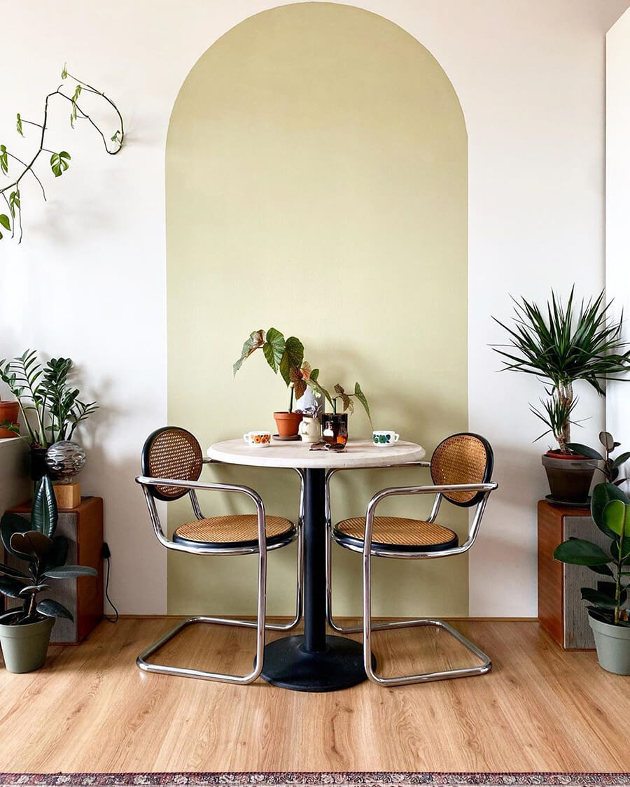 Un comedor pequeño para dos personas con un arco pintado en la pared que le da mucho estilo.