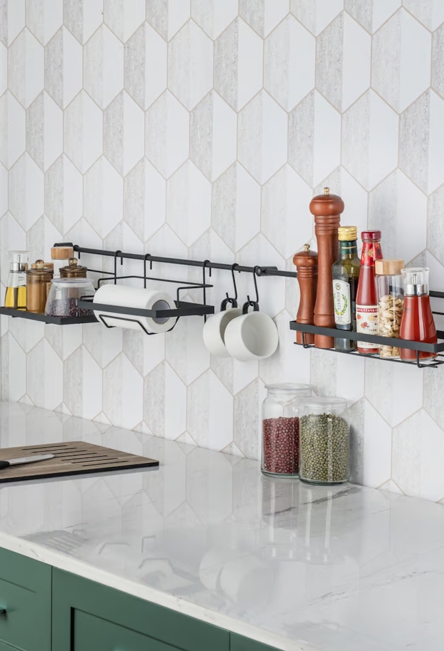 Detalle de una pared y cubierta de cocina blancas, en la pared hay 3 organizadores de pared con especias, tazas, toalla de papel y y condimentos varios.