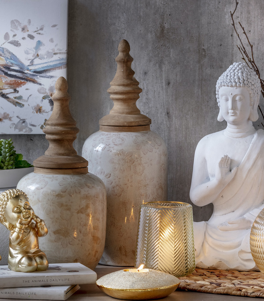 Detalle de una mesa de estilo zen. Hay un buda blanco, dos jarrones de cerámica con tapas altas, un pequeño buda dorado y velas