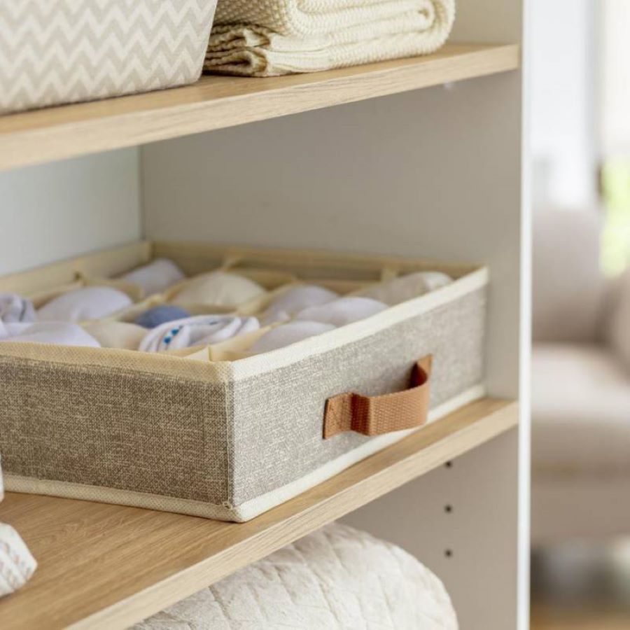 Clóset abierto con repisas de madera. En una de ellas hay un organizador de tela con secciones para guardar la ropa interior. Es de color gris con una manilla café. En las otras repisas hay ropa de cama y cajas organizadoras.